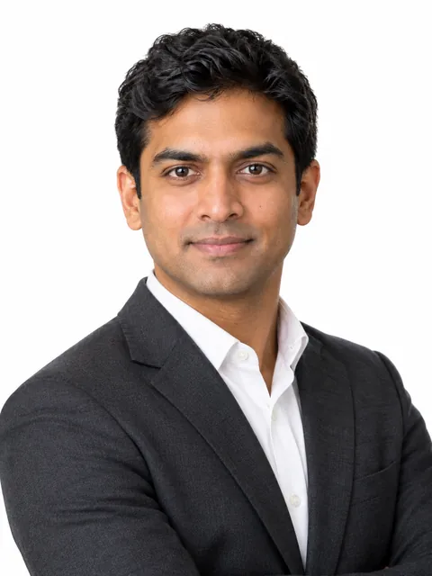 Fictional South Asian man wearing a charcoal blazer in a professional headshot against a light background